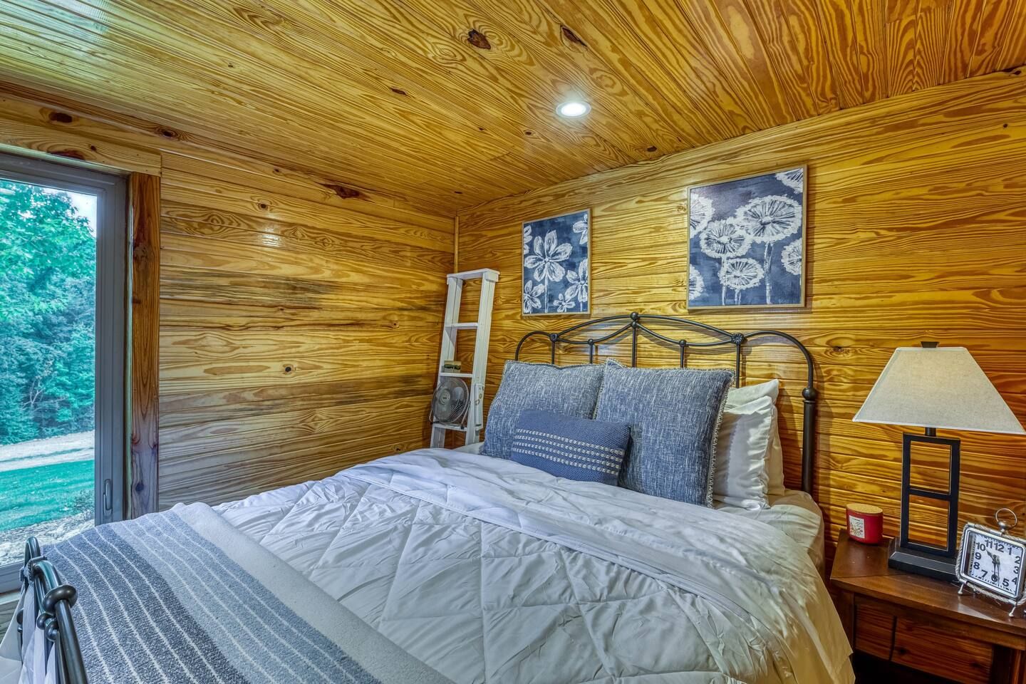 Bedroom with wood walls and ceiling, bed with blue accents, open doorway.