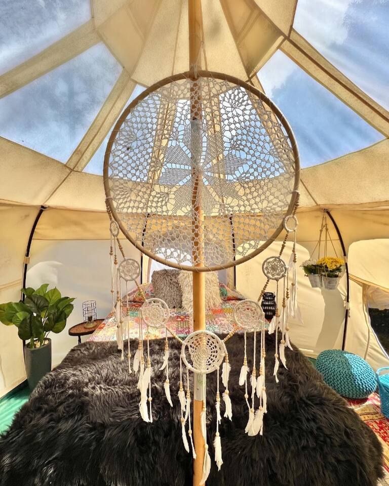 Inside a glamping tent, a large dreamcatcher hangs above a bed with a black fur cover.