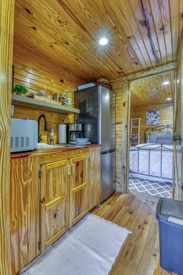 Small rustic kitchen with wood paneling, cabinets, and appliances; doorway leads to bedroom.
