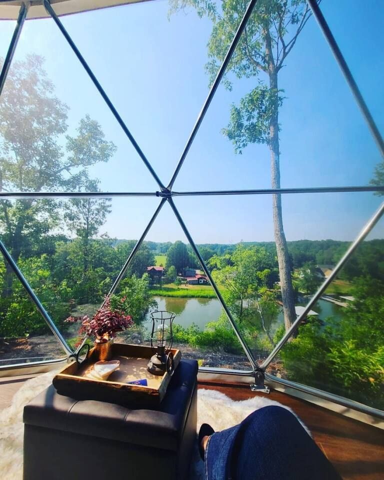 View from a dome-shaped window of a lake, trees, and small buildings. A tray and ottoman are visible indoors.