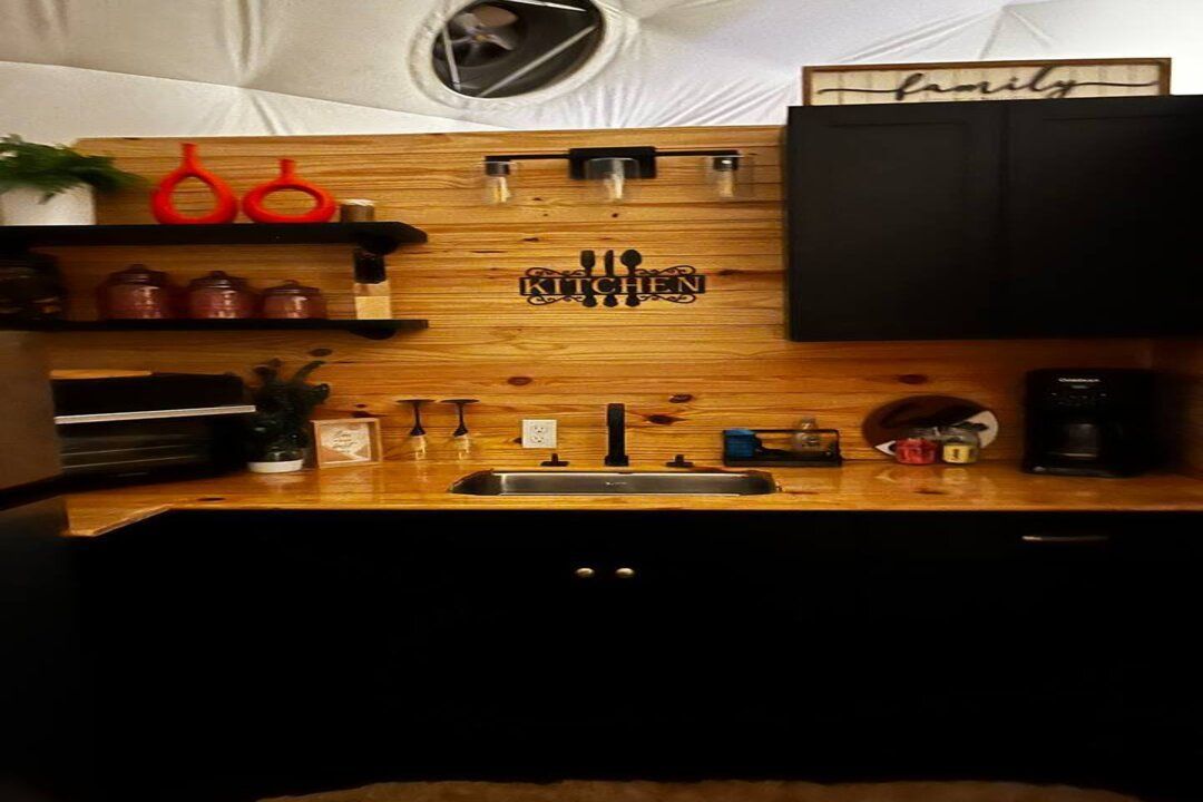Kitchen with black cabinets, wooden backsplash, sink, and shelves with décor.