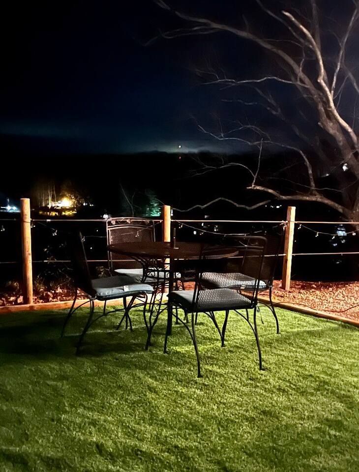 Patio table and chairs on artificial grass at night with a distant view of lights.