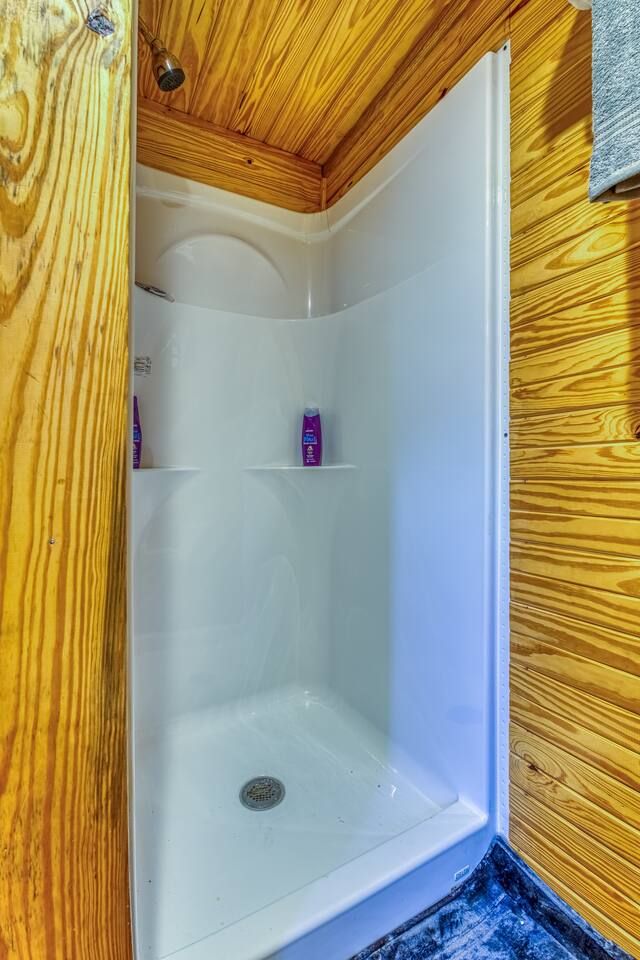 White shower stall inside a wood-paneled room.  Purple shampoo bottles are visible on a shelf.