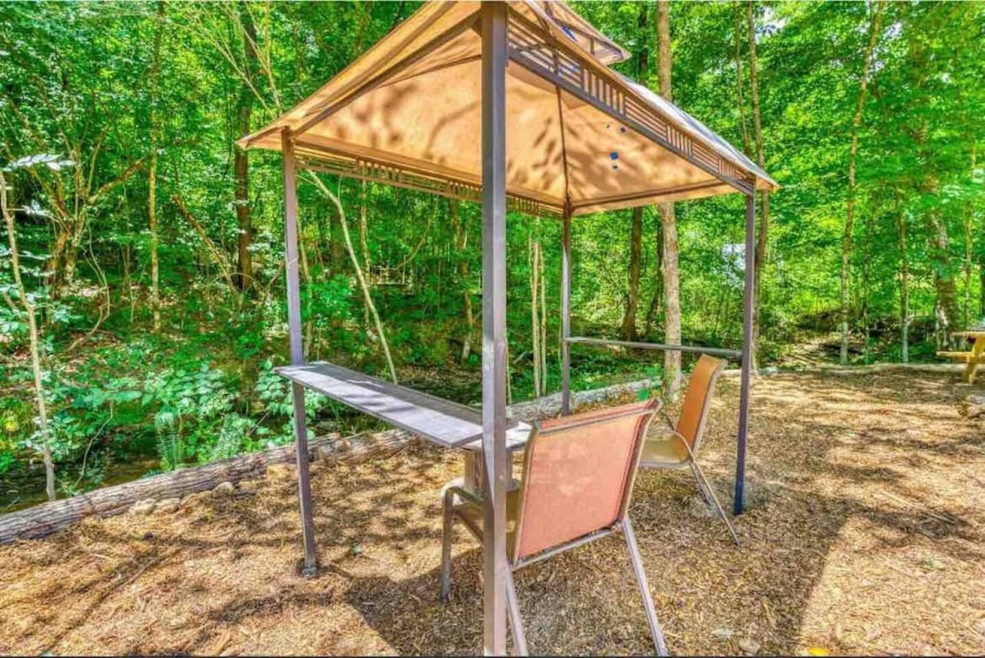 Gazebo with table and chairs in a forest clearing.