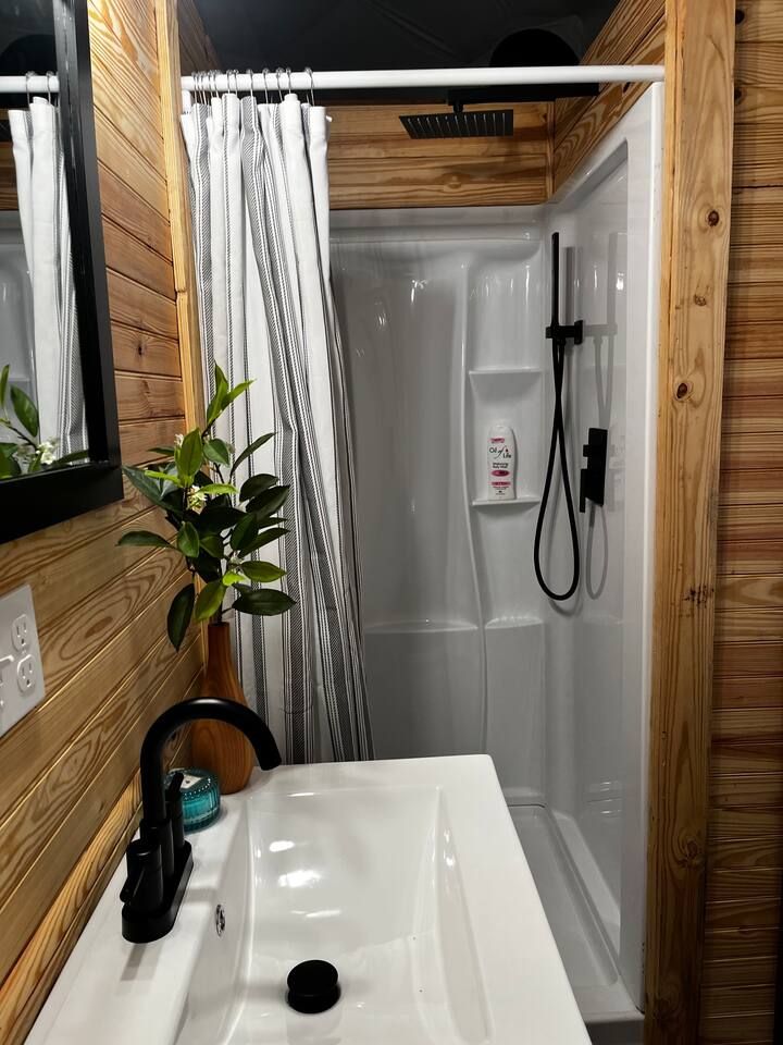 Bathroom with a white sink, shower, and striped curtain. Wood paneling on walls.