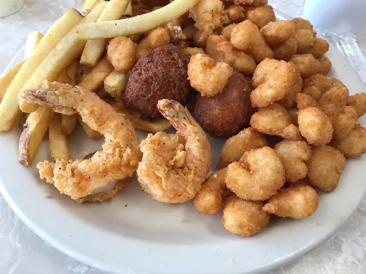 Plate of fried seafood with french fries, shrimp, hushpuppies.