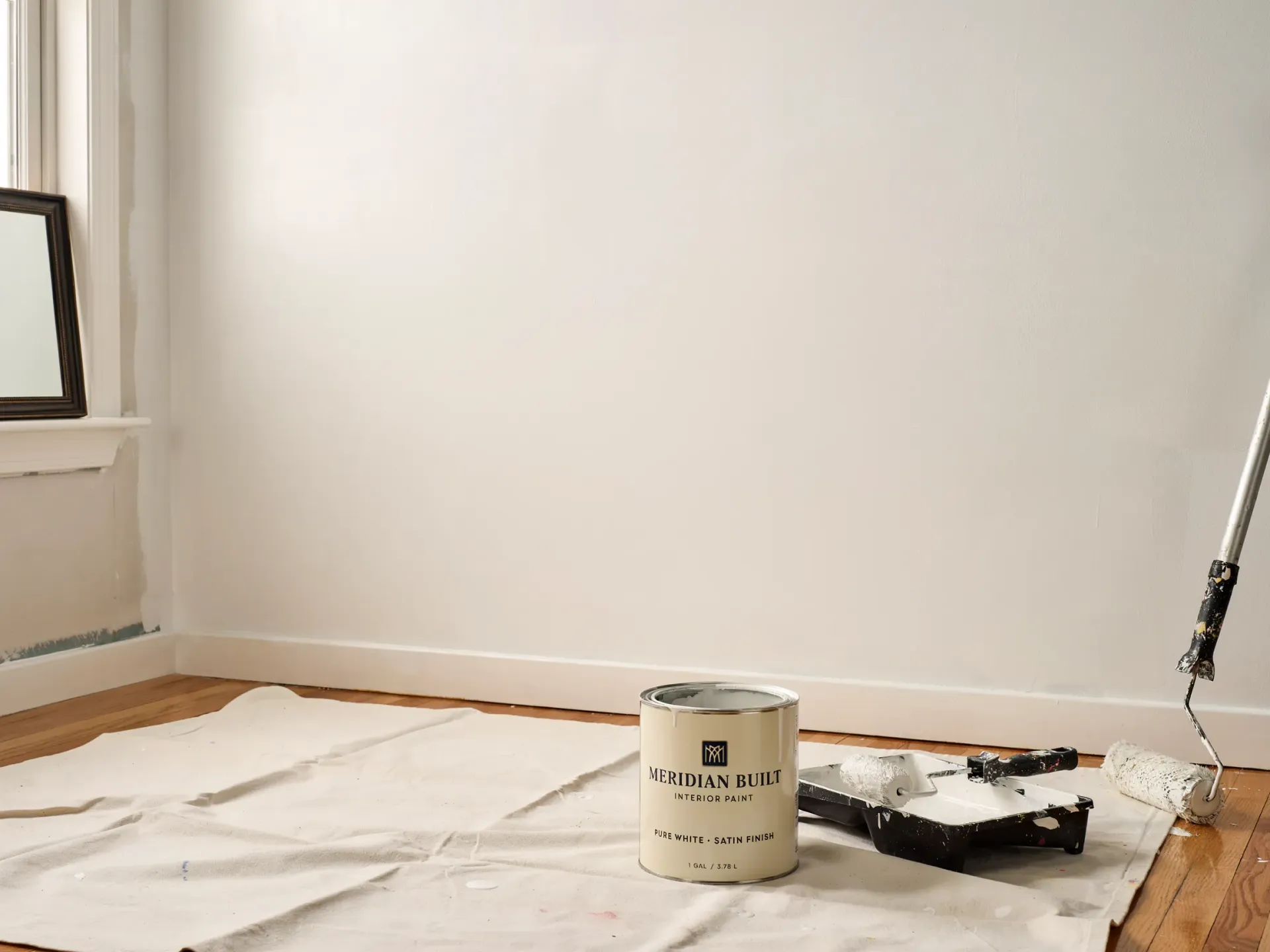 Empty room with drop cloths on the floor, painting supplies, and a paint can near the wall