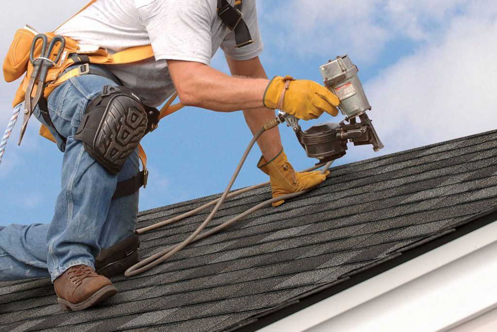 Worker installing shingles on a rooftop with a nail gun and tool belt