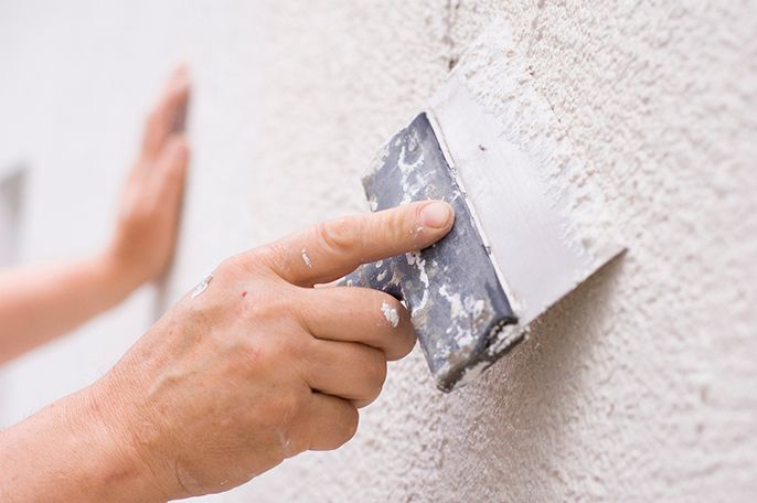 Hand using a putty knife to smooth plaster on a white wall