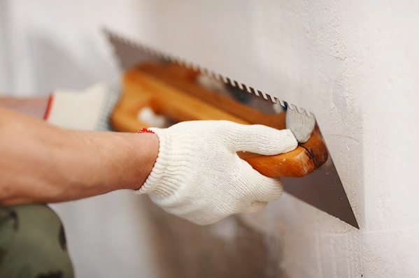 Hand in white glove spreading plaster on a wall with a trowel