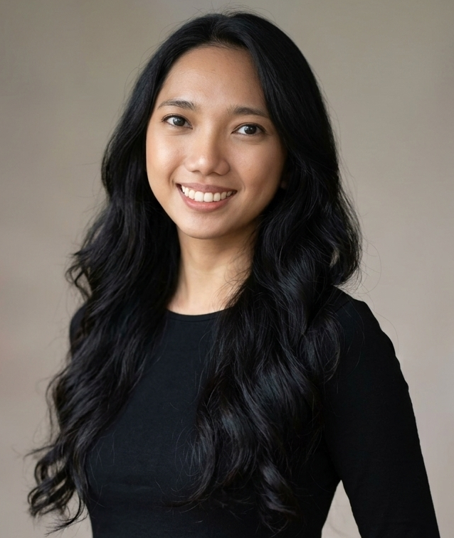 Smiling woman with dark hair, wearing black top, gold necklace, against a gray background.