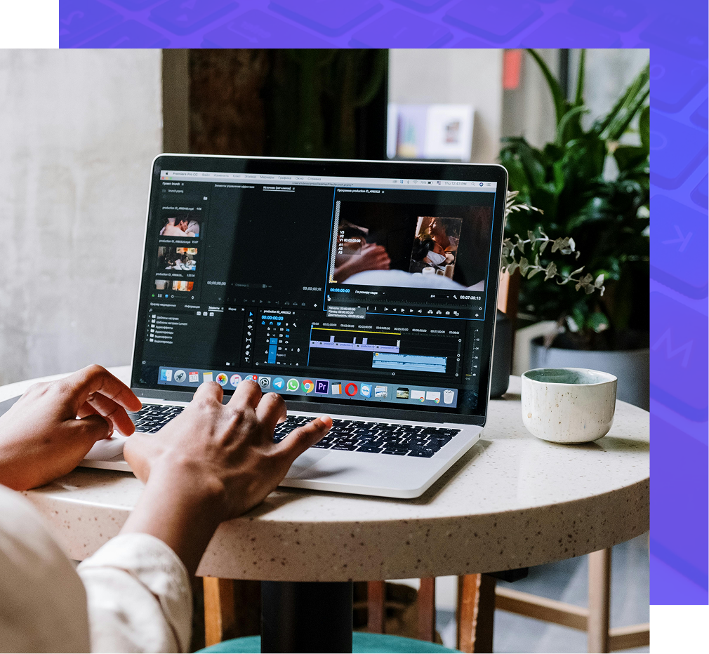 Person editing video on a laptop, hands on keyboard, sitting at a round table with a mug and plants.