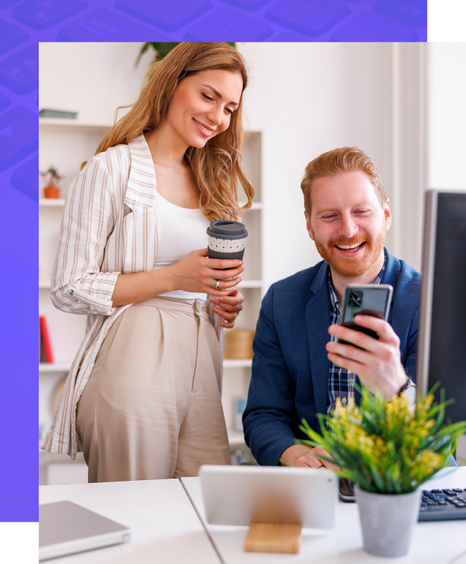 Woman and man looking at phone, smiling. Office setting, potted plant, coffee cup, tablet.