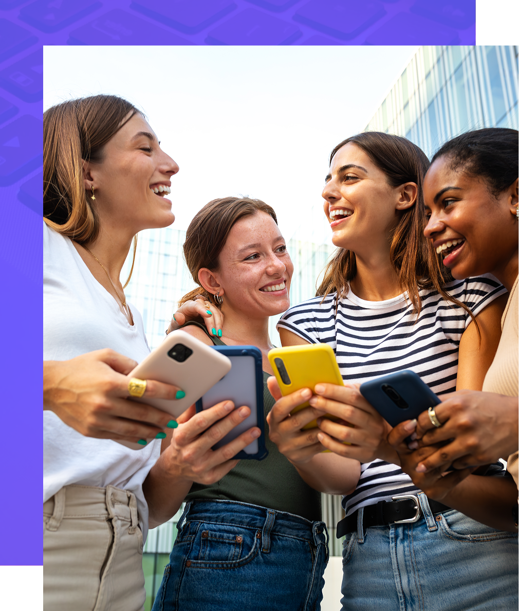 Four people laughing and looking at their phones outdoors.