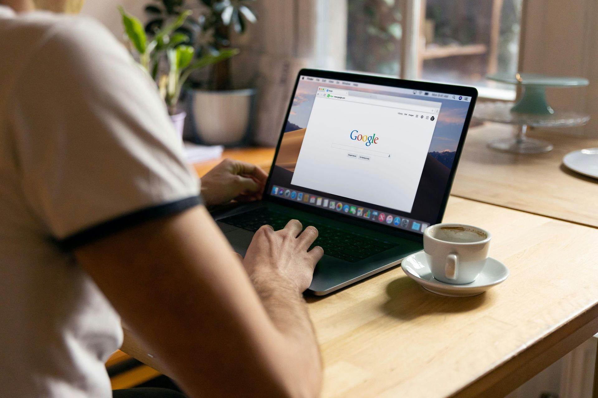 Person using a laptop at a wooden table with a cup of coffee beside it