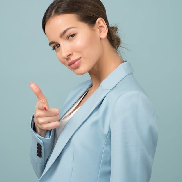 A woman in a light blue jacket is giving a thumbs up