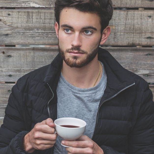 A man in a black jacket is holding a cup of coffee