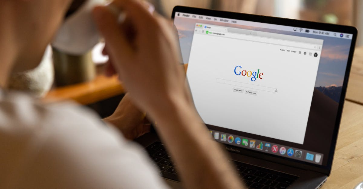 A person is using a laptop computer while holding a cup of coffee.