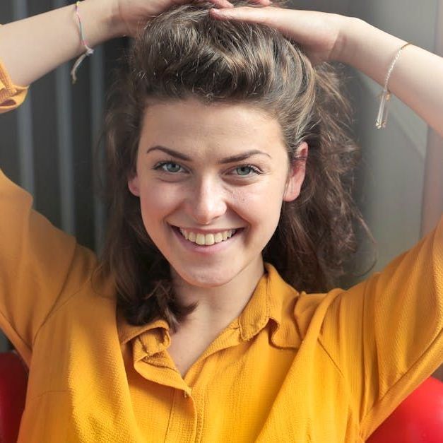 A woman in a yellow shirt is smiling and holding her hair in a bun.