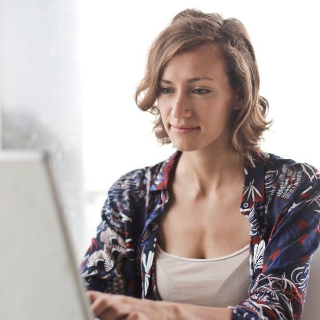 A woman in a floral shirt is typing on a laptop