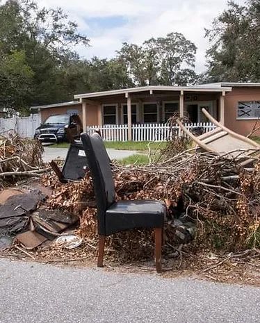 A chair is sitting in front of a pile of branches in front of a house.