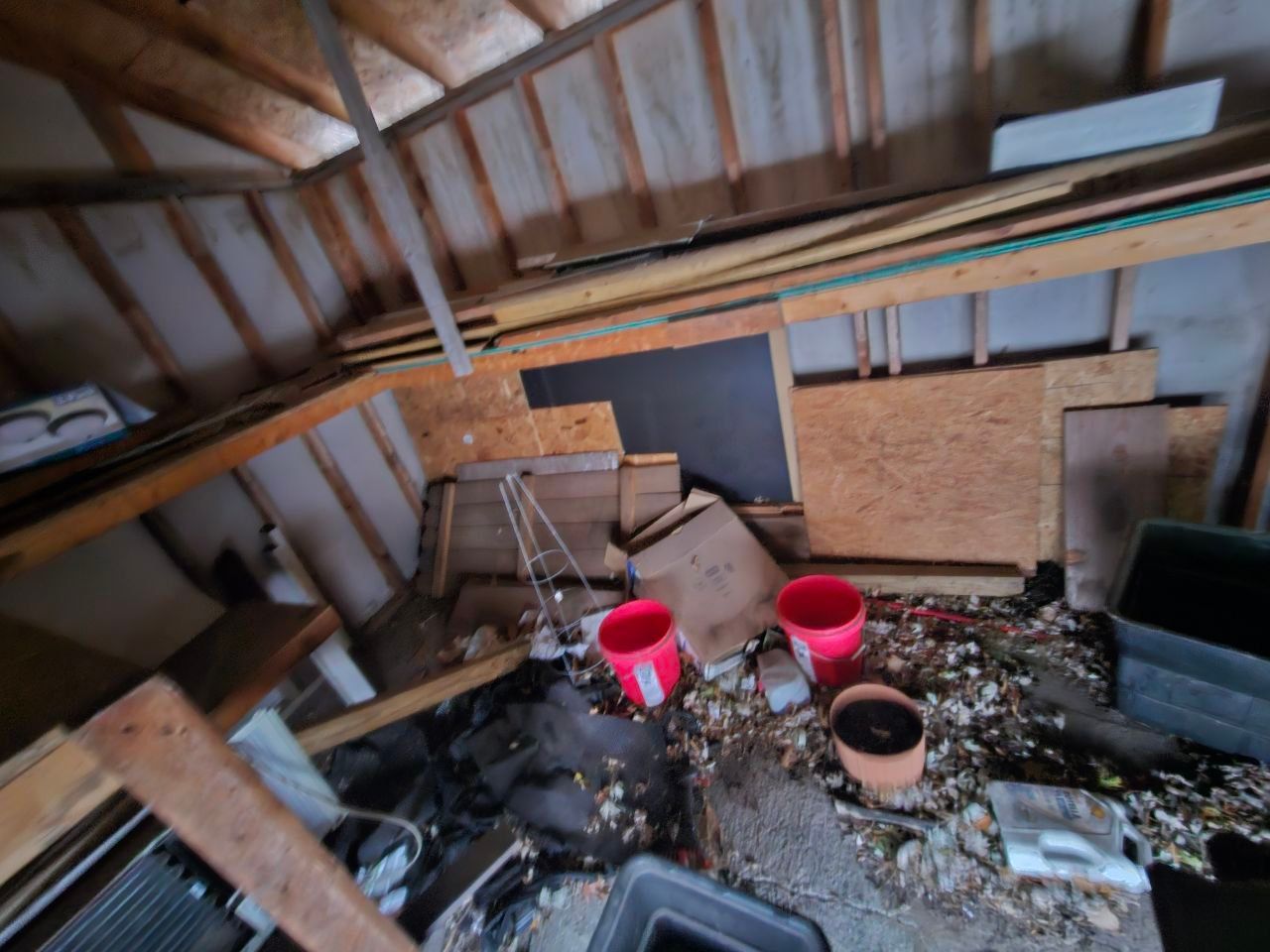 A room with a lot of junk in it and two red buckets on the floor.