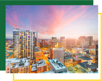 High-angle view of a city skyline at sunset, with golden light reflecting off modern buildings and orange-tinted clouds.