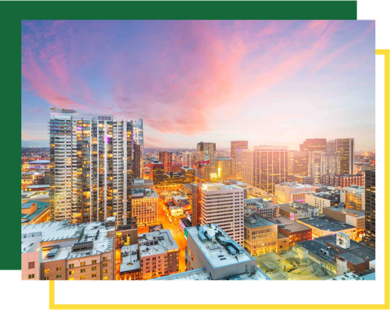 A vibrant, high-angle sunset view of a densely built city skyline with glowing windows and warm evening light.