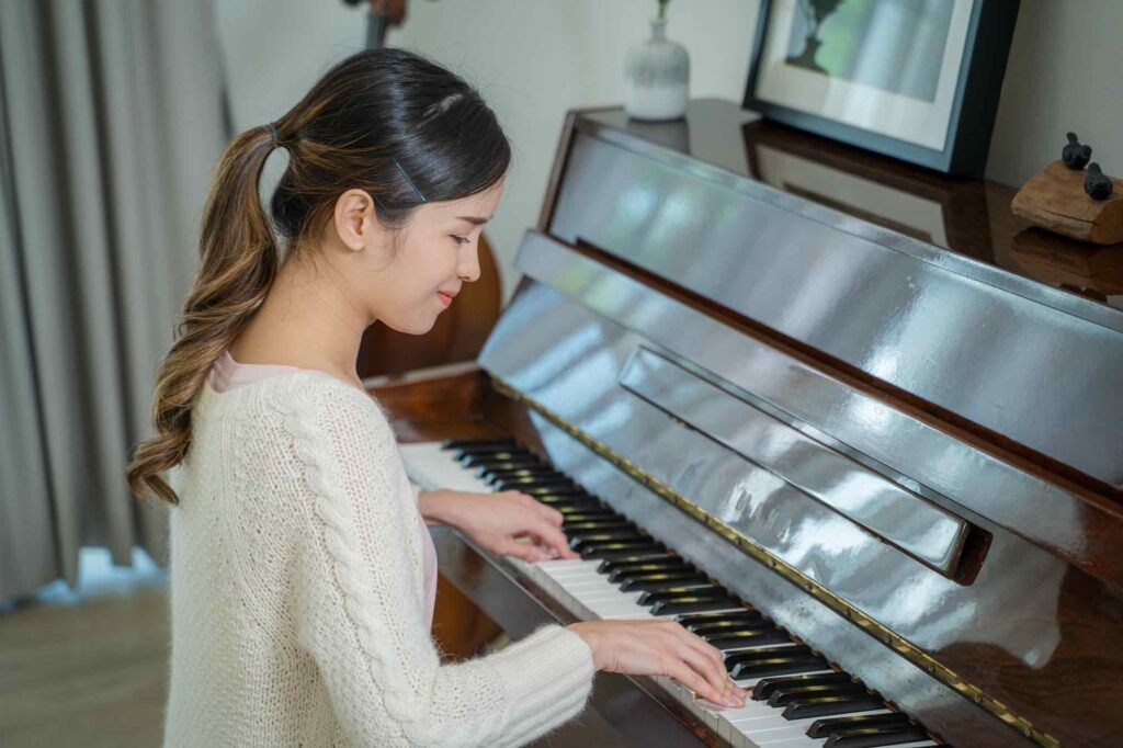 A person in a cream cable-knit sweater playing the piano in a brightly lit room.