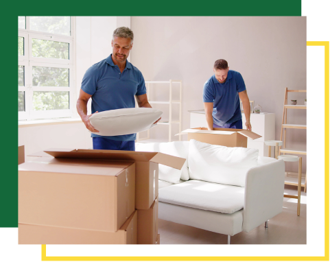 Two people in blue shirts pack belongings into cardboard boxes in a bright, modern living room with a white sofa.
