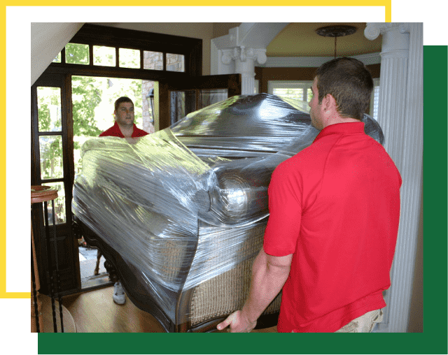 Two people in red shirts move a large sofa wrapped in clear plastic through an open doorway.