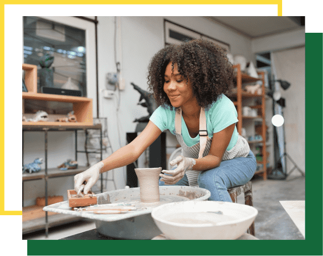 A person wearing an apron crafts a clay vessel on a pottery wheel in a studio.