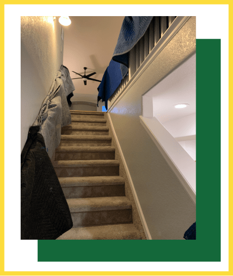 A carpeted staircase leading upward with protective moving blankets draped over the railings and walls.