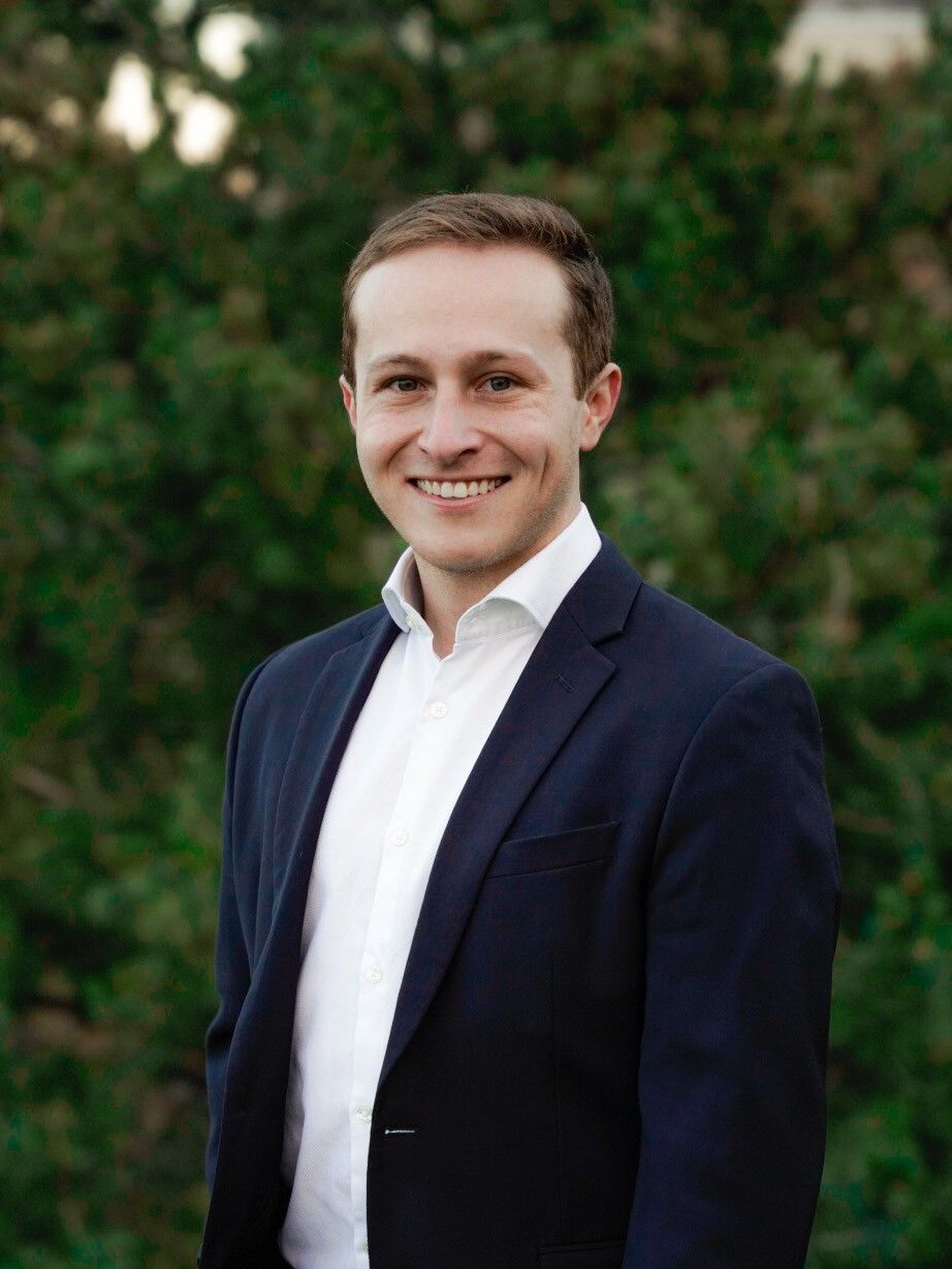 A man in a blue shirt and black pants is standing with his hands in his pockets.