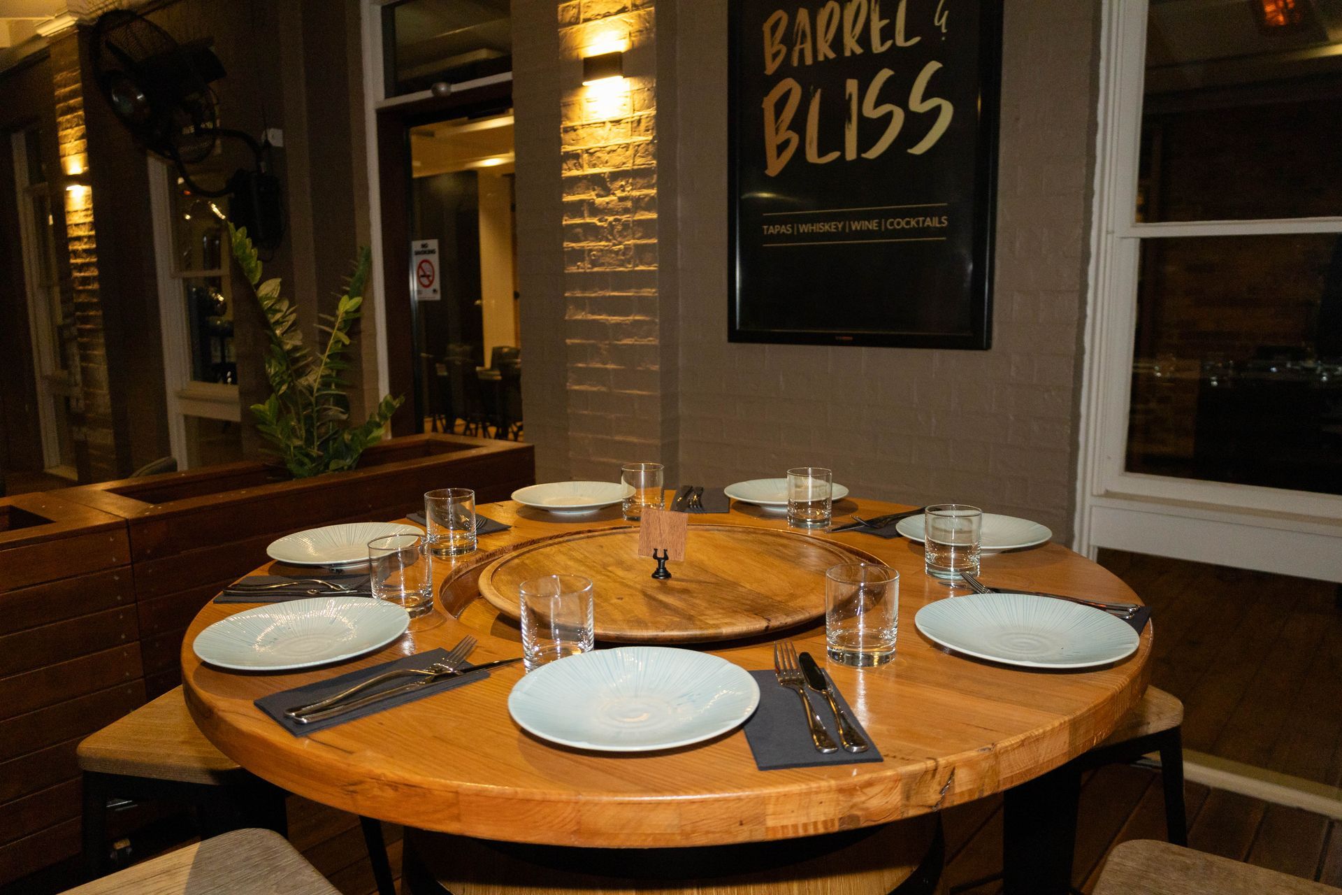 A round wooden table set for a meal, with plates, glasses, and silverware at a restaurant.