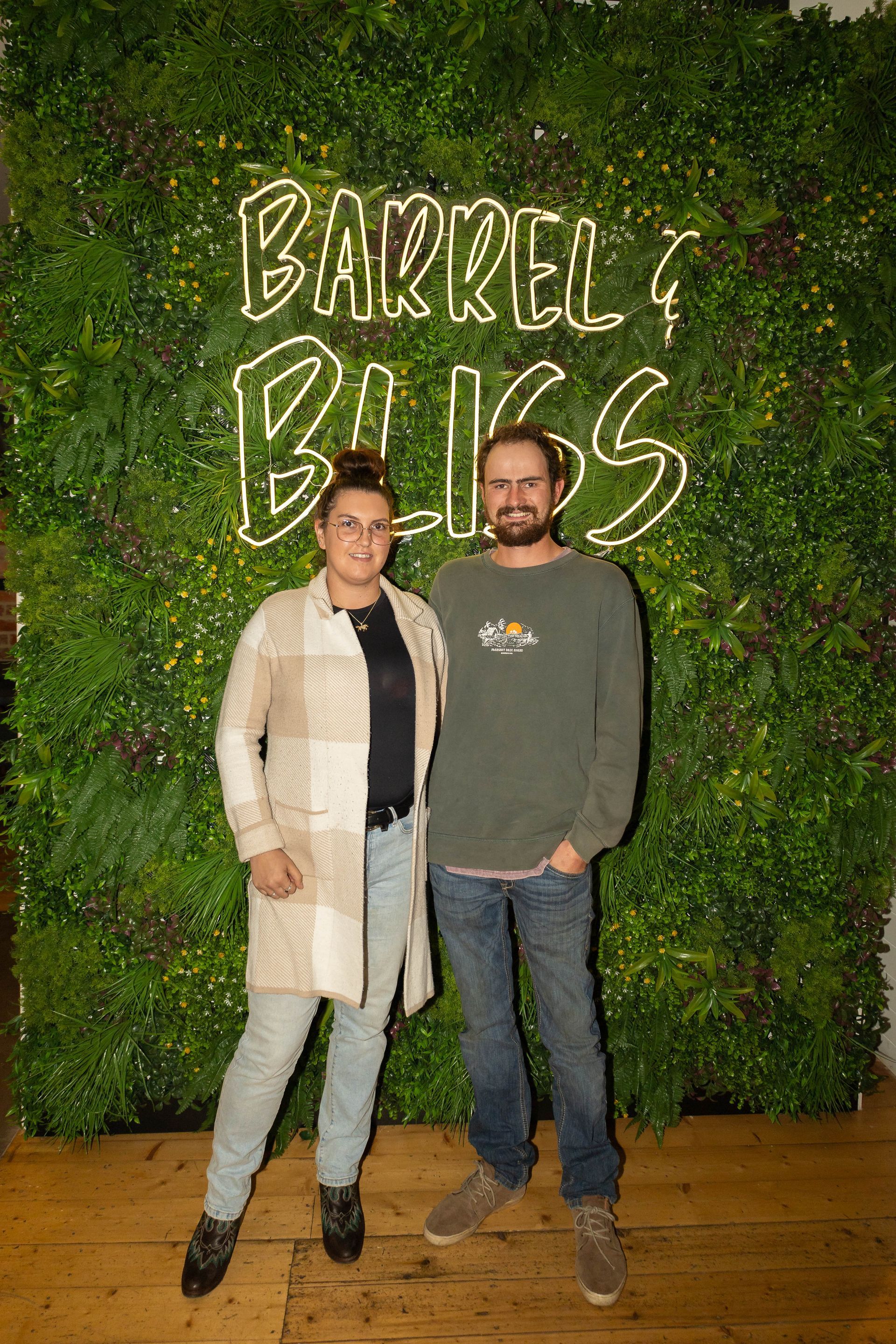 Two people pose in front of a green wall with a neon 