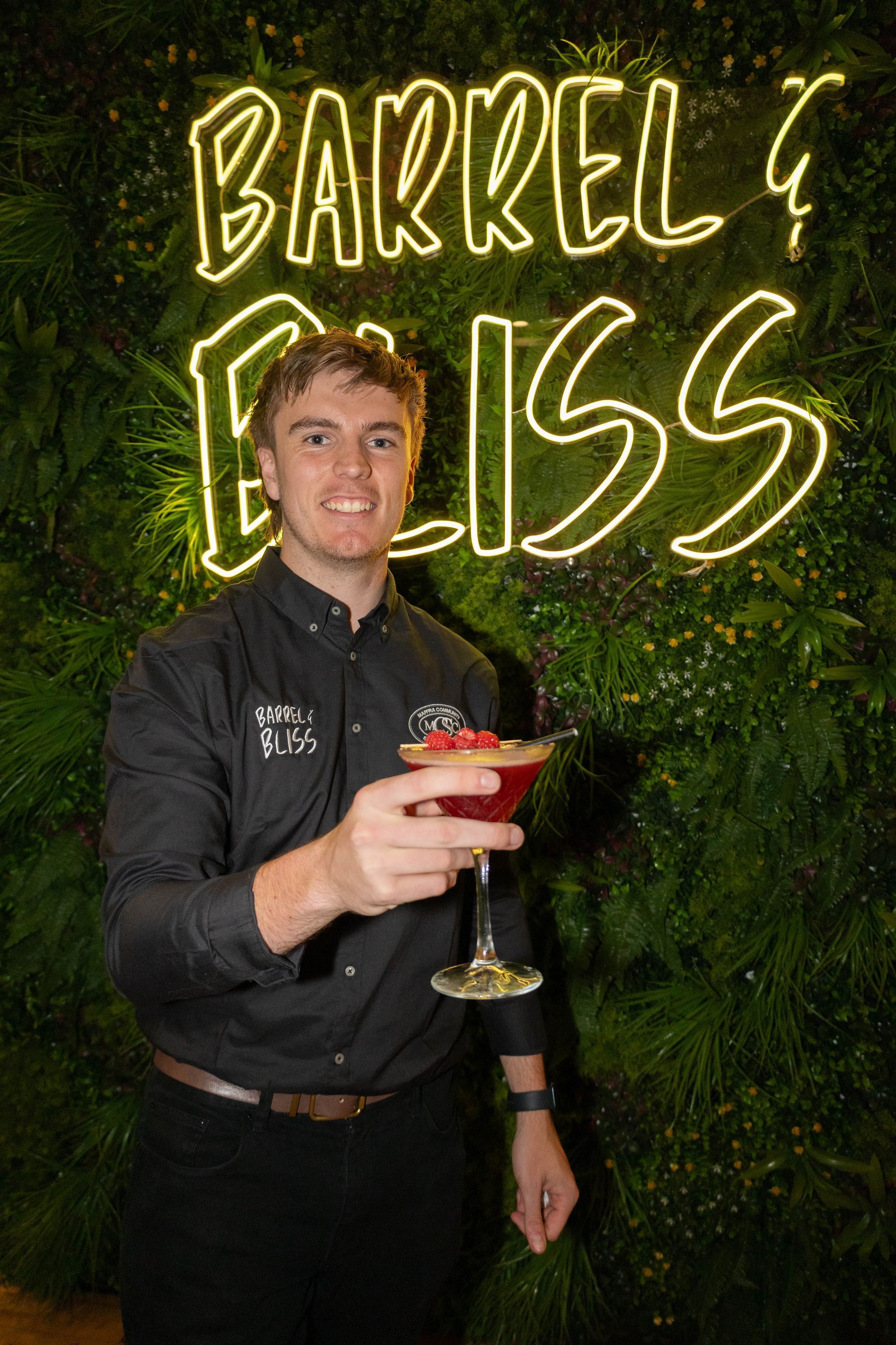 Man in black shirt holding a red cocktail in front of 