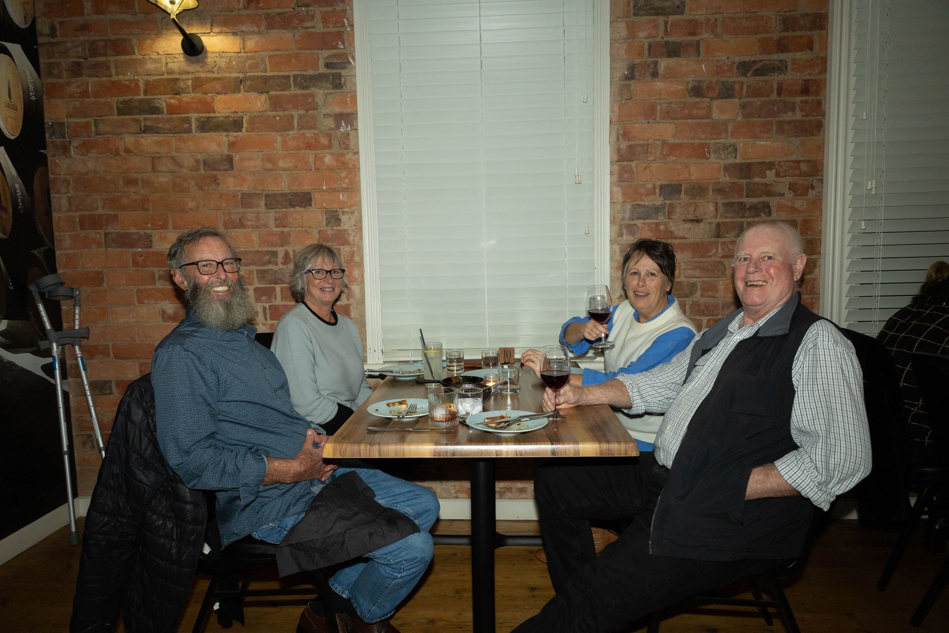 Four people seated around a table in a restaurant, brick wall background, holding drinks.