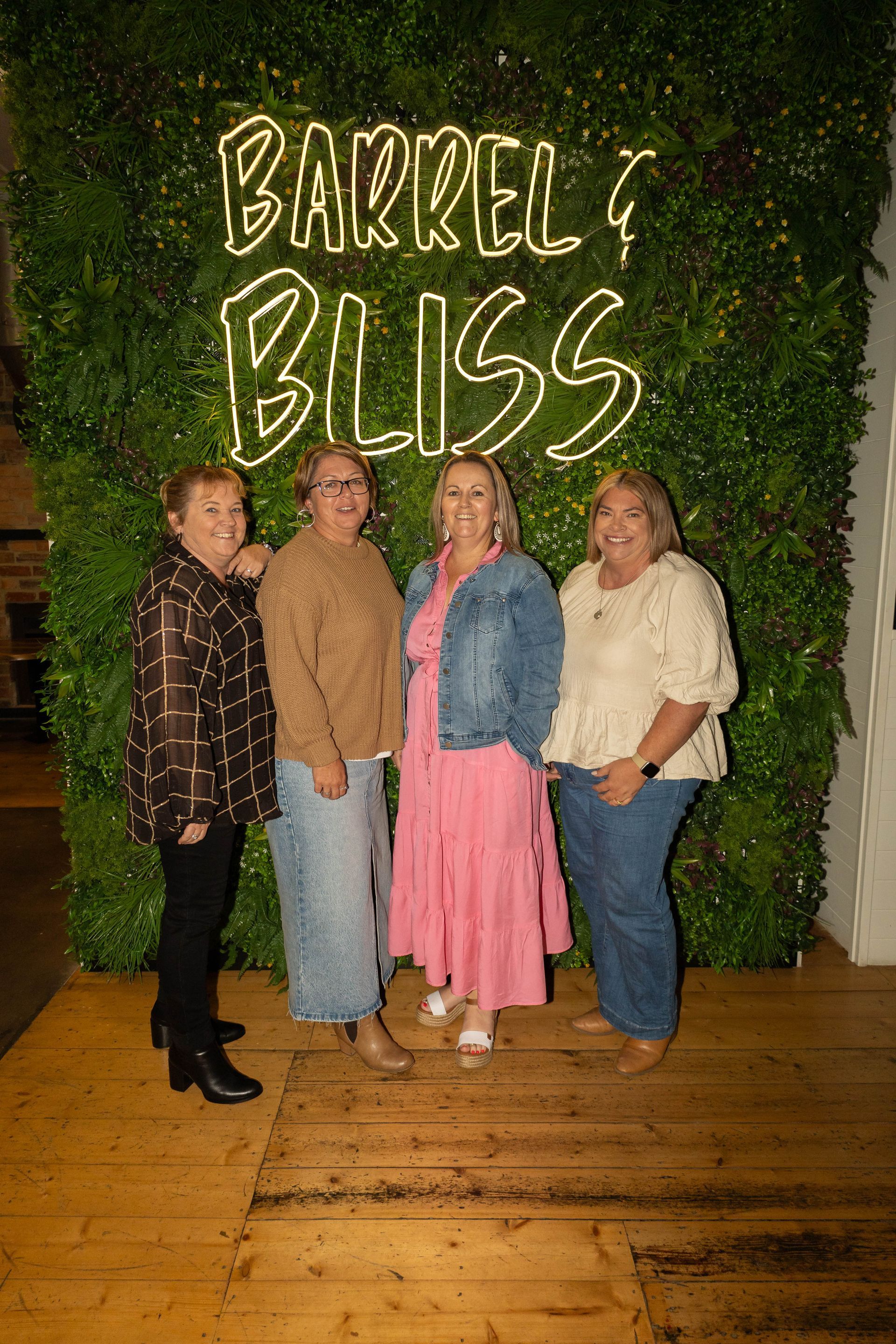 Four women smiling in front of a wall with a 