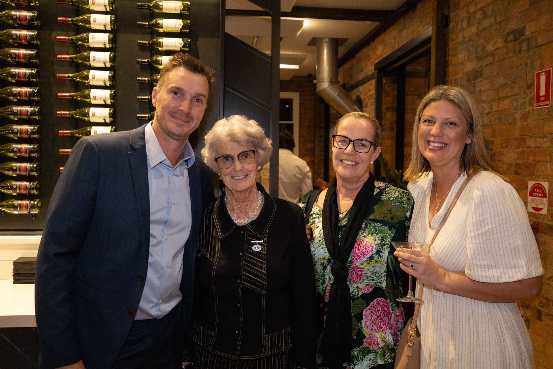 Four people smiling at a winery. A man, a woman, another woman with glasses, and a blonde woman with a glass.
