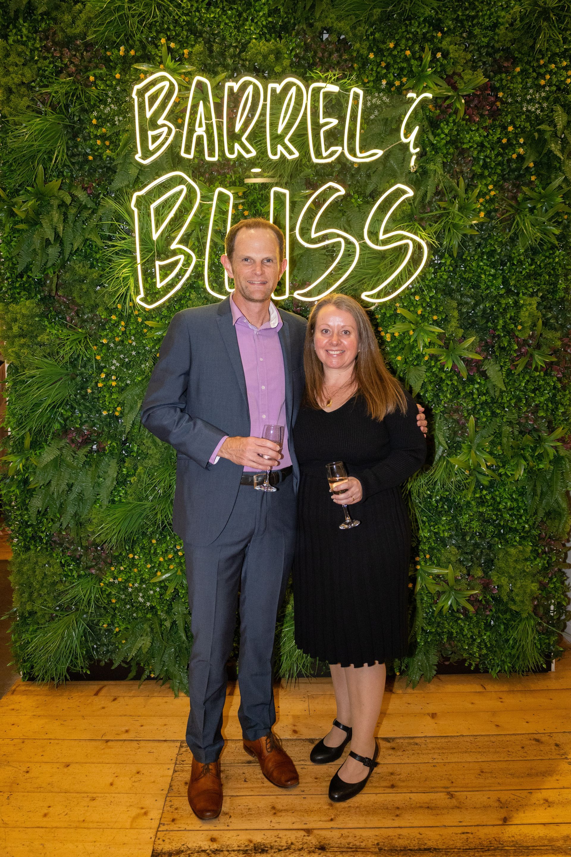 Man and woman smiling, holding drinks, in front of 