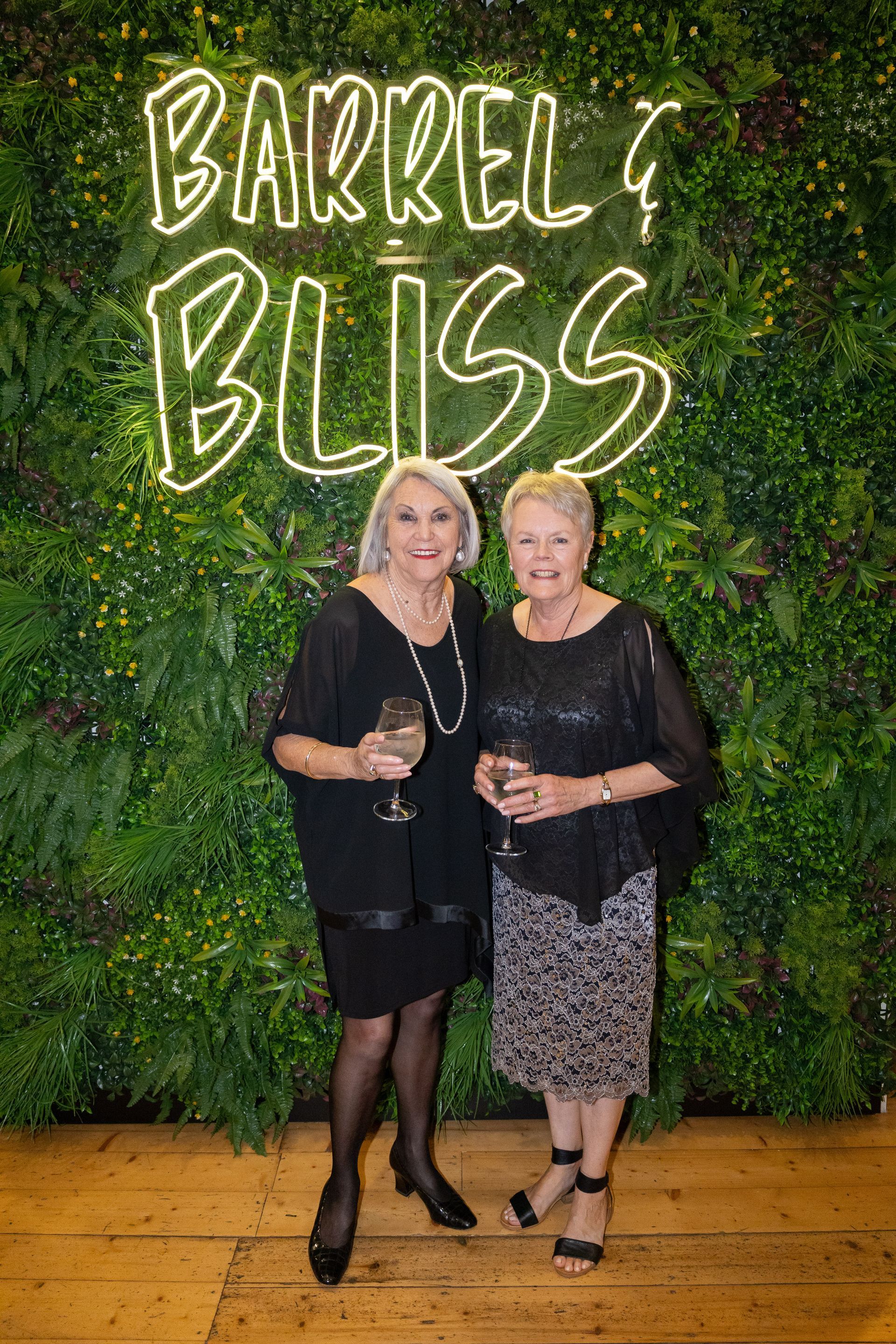 Two women smiling, posing in front of a green wall with 