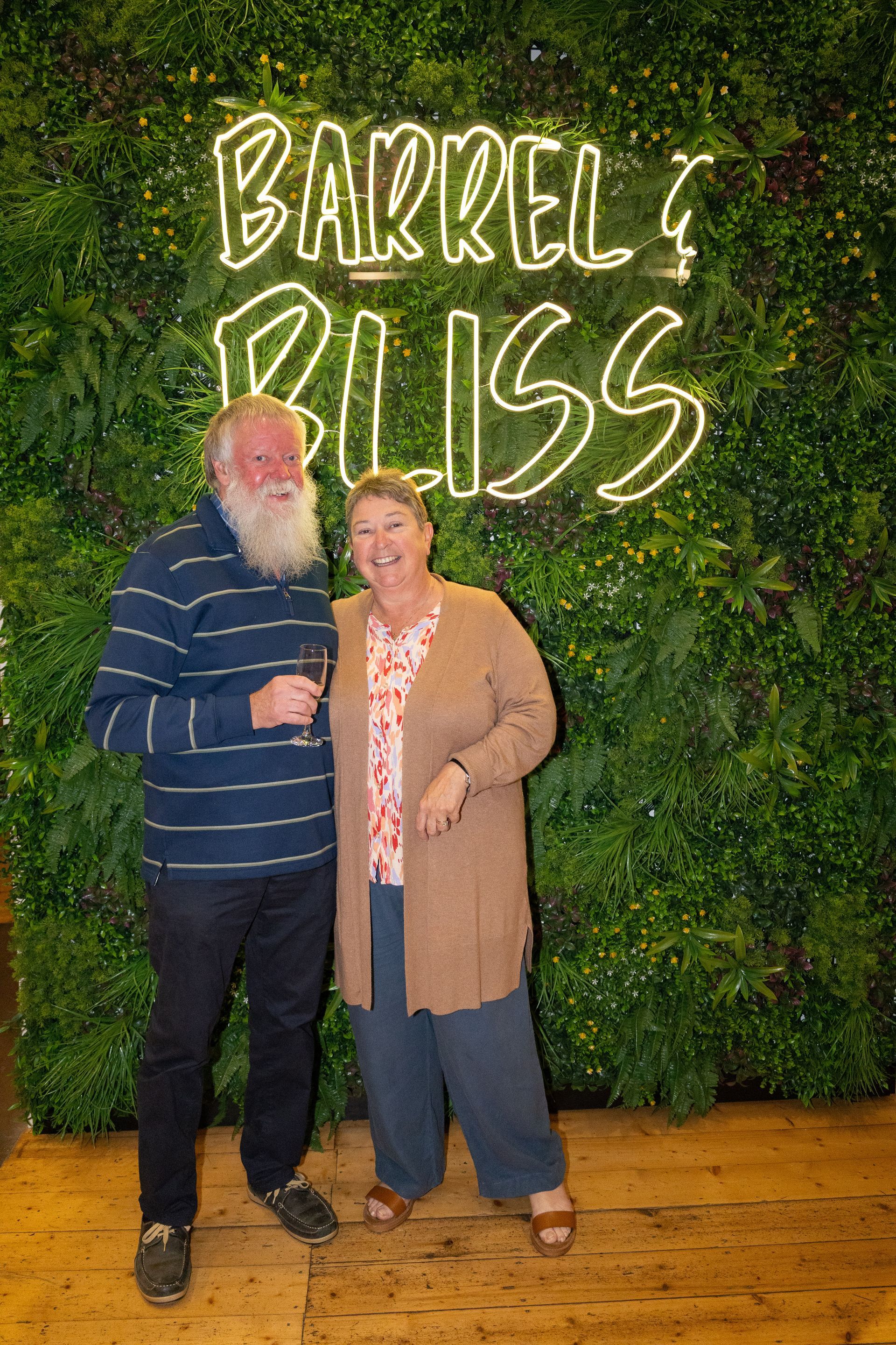 Couple smiles in front of a green wall with neon 
