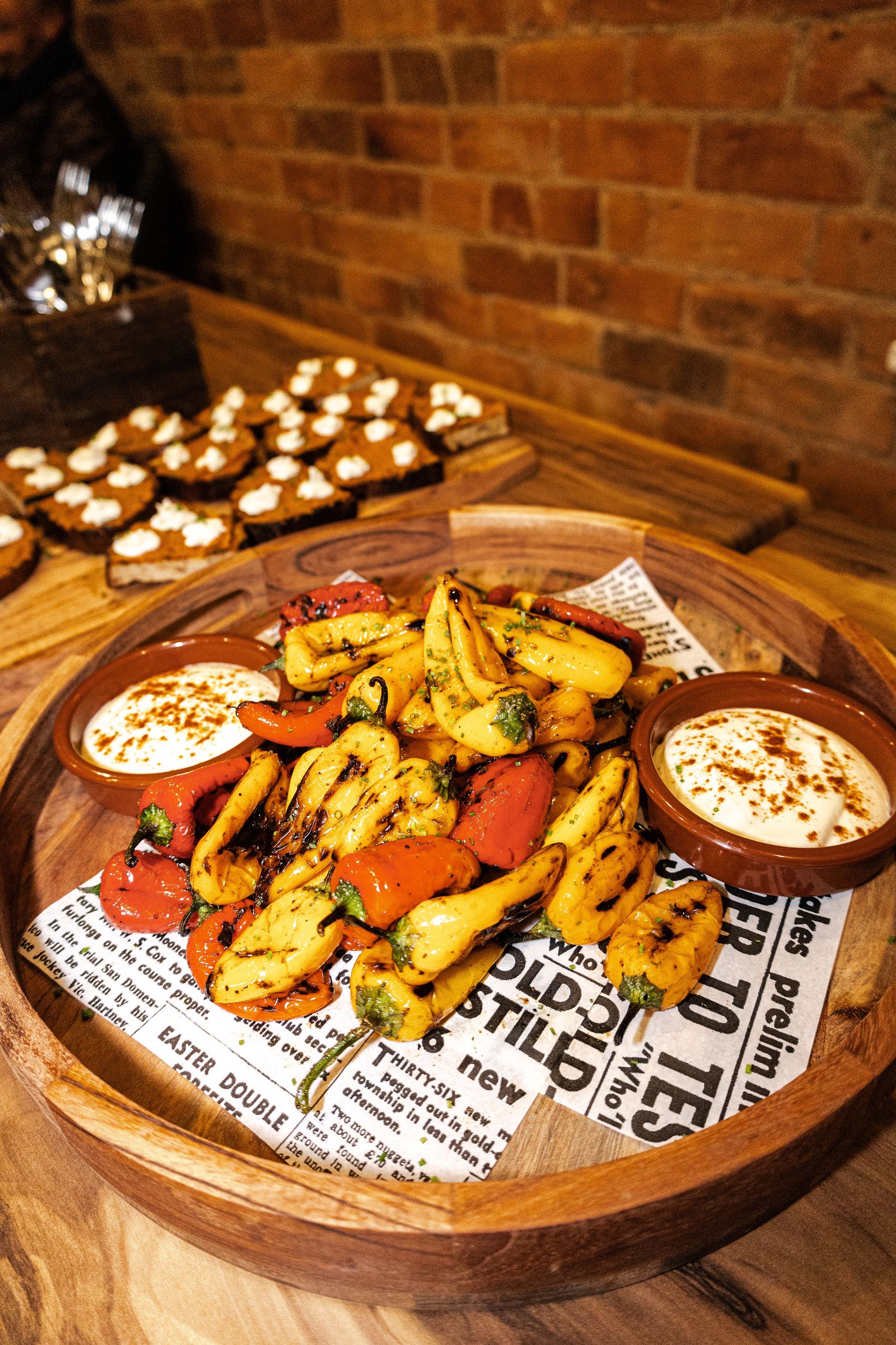 Grilled peppers with dipping sauces in a wooden bowl, brick wall background.