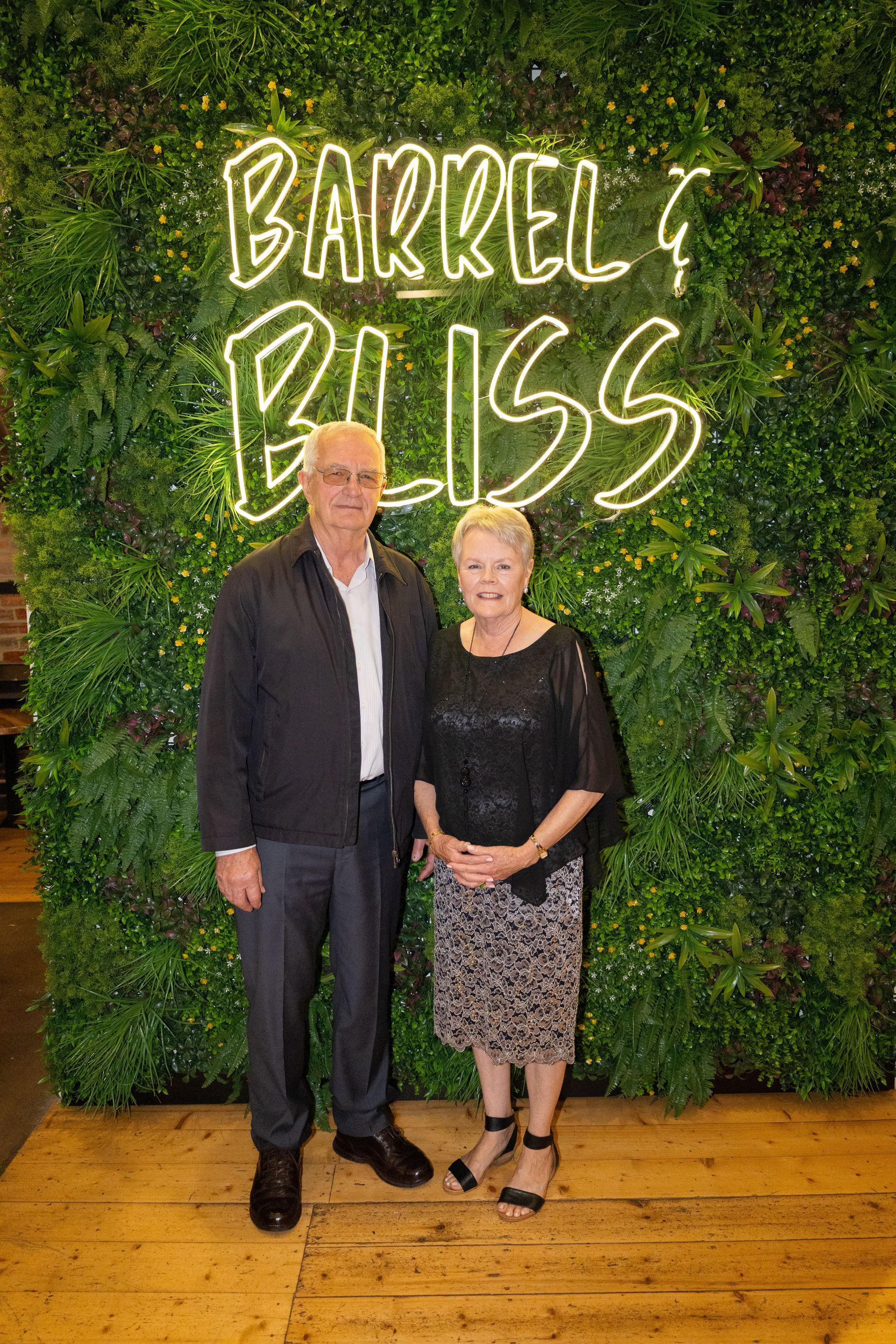 Man and woman pose in front of a green wall with neon 