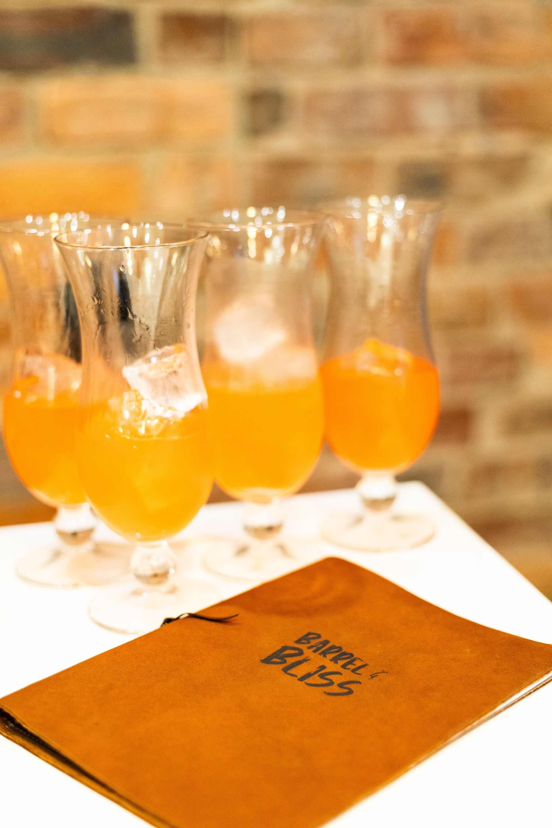 Orange drinks in hurricane glasses with menu on a table. Brick wall background.
