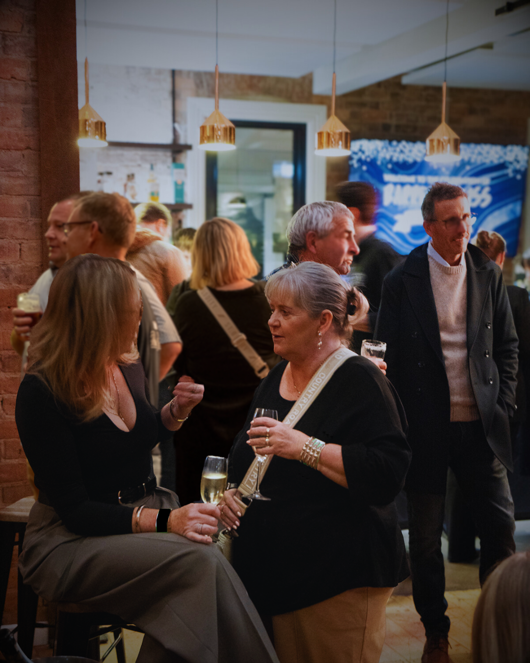 People socializing indoors; drinks in hand, brick wall background, modern lighting.