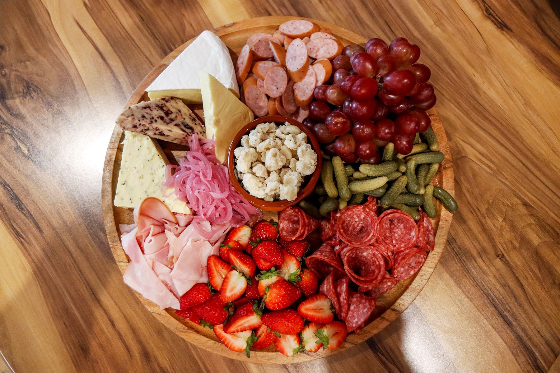 Charcuterie board with cheese, meats, fruit, and pickled vegetables on a wooden surface.
