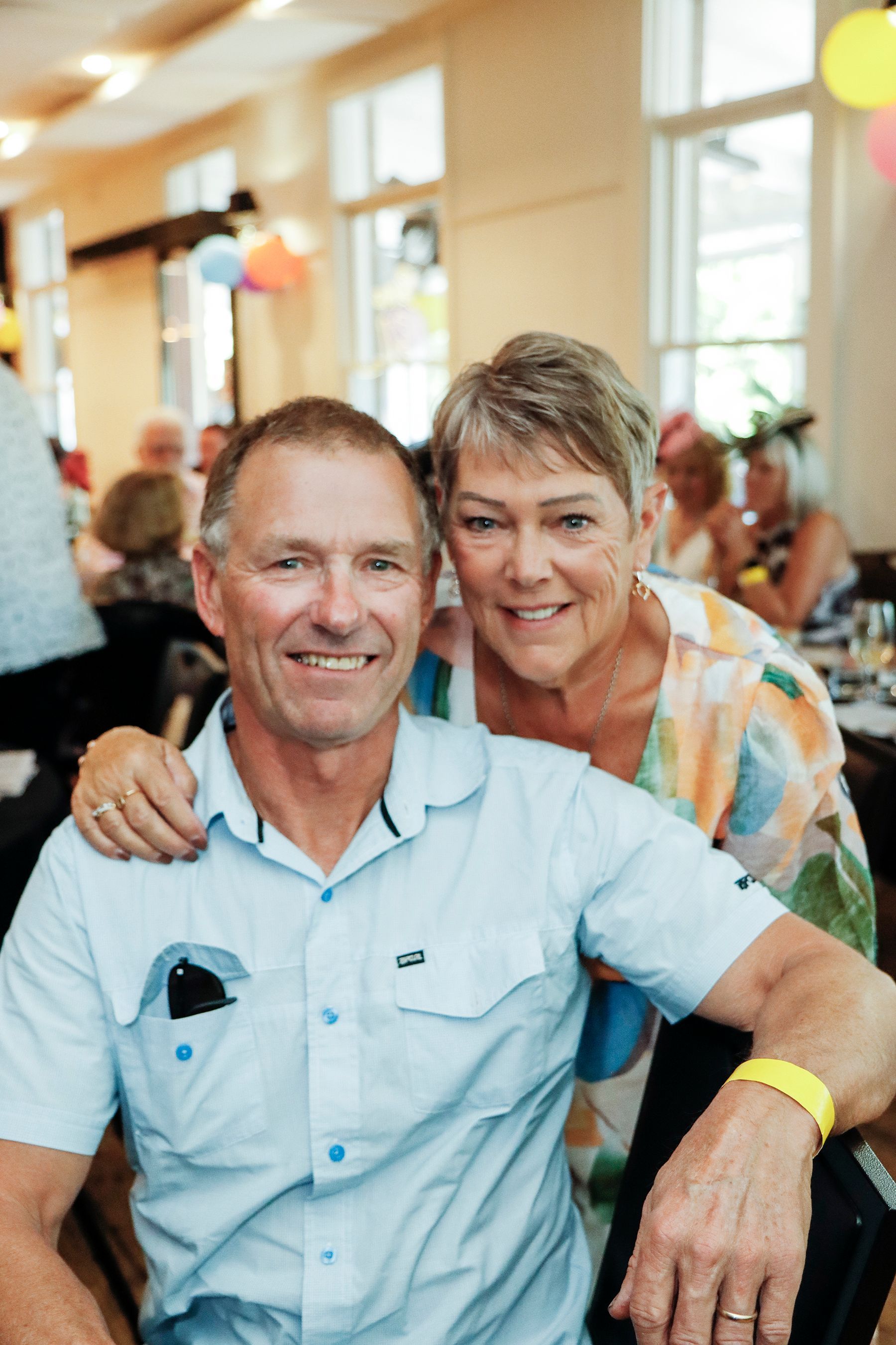Smiling couple posing at a party; man in blue shirt, woman with arm around him.
