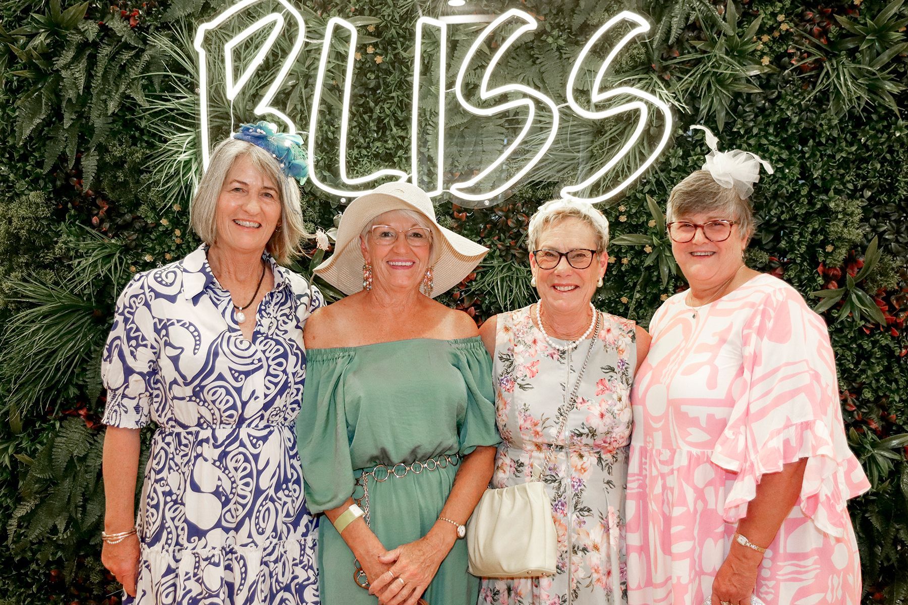 Four women in hats pose in front of a 